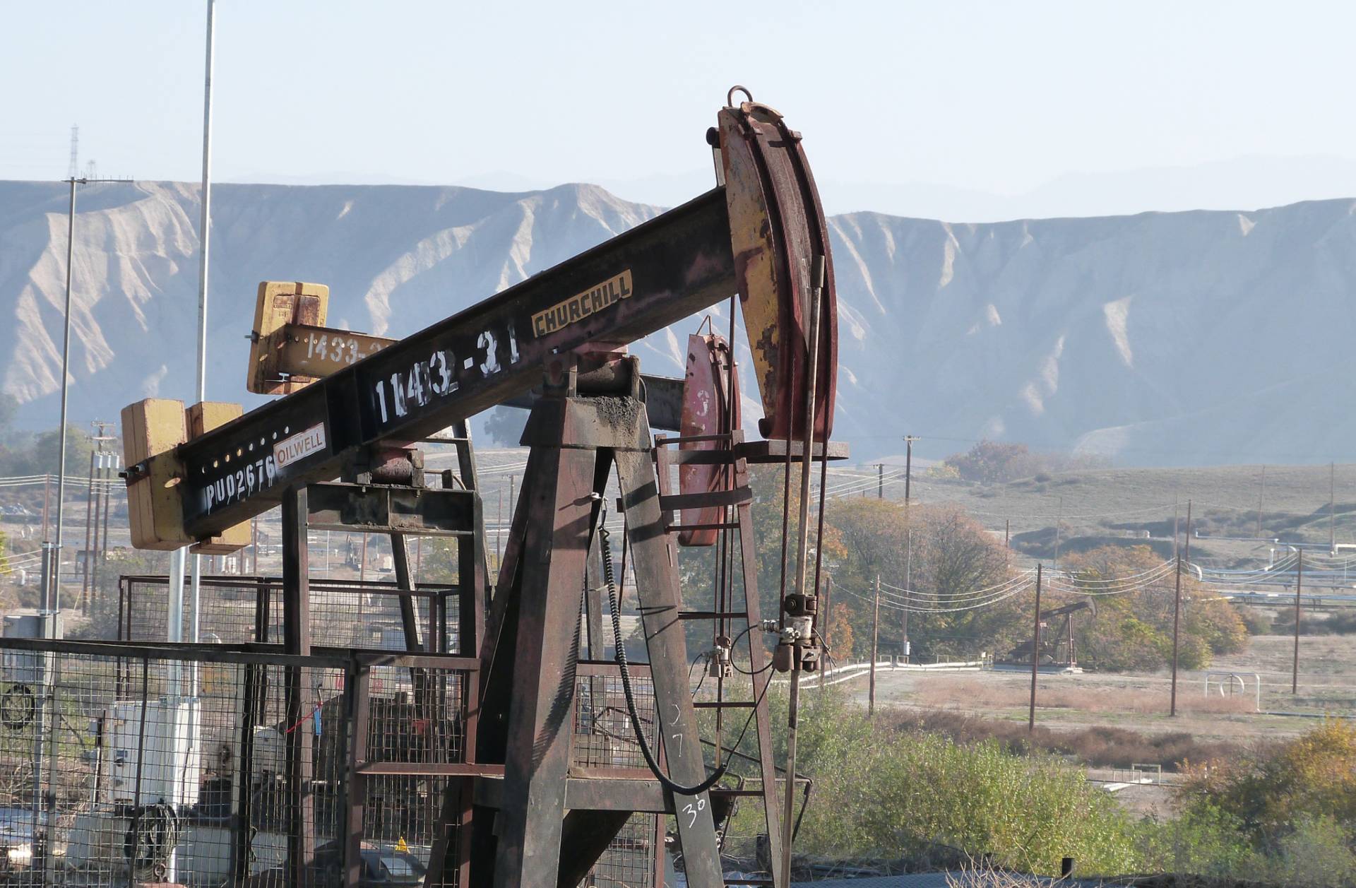A large, rusty metal pump jack, with the Bluffs in the background, in Chevron's Kern River Oil Field, near Bakersfield, California.