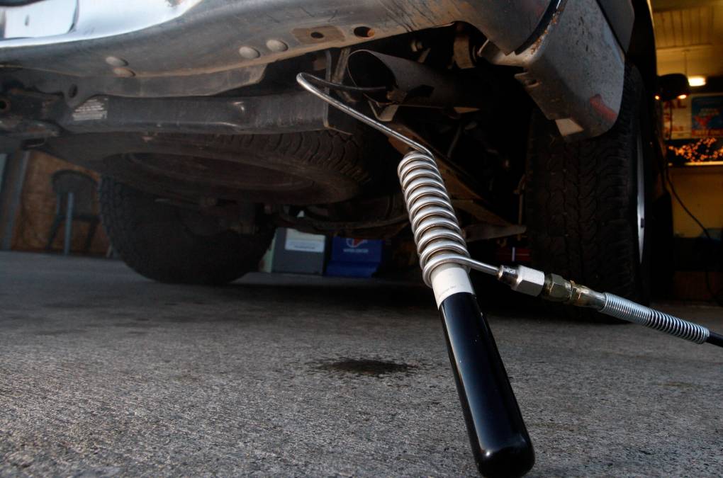 A metal probe with a coiled wire around it extends into the tailpipe of a car with a rusty underbelly.