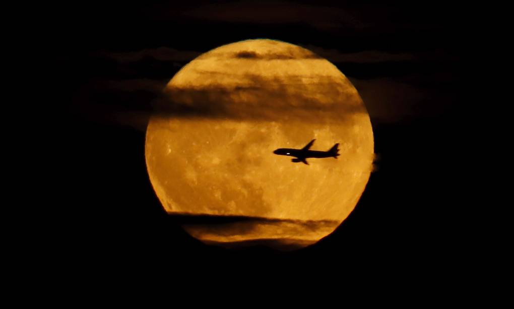 An airplane flies past the full, bright, dark yellow-toned Sturgeon Supermoon as it rises above New York City on August 11, 2022, as seen from West Orange, New Jersey. (Photo by Gary Hershorn/Getty Images)