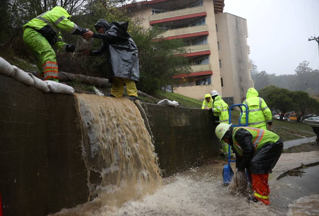 Workers in yellow rain gear try to divert mud brown flood water.