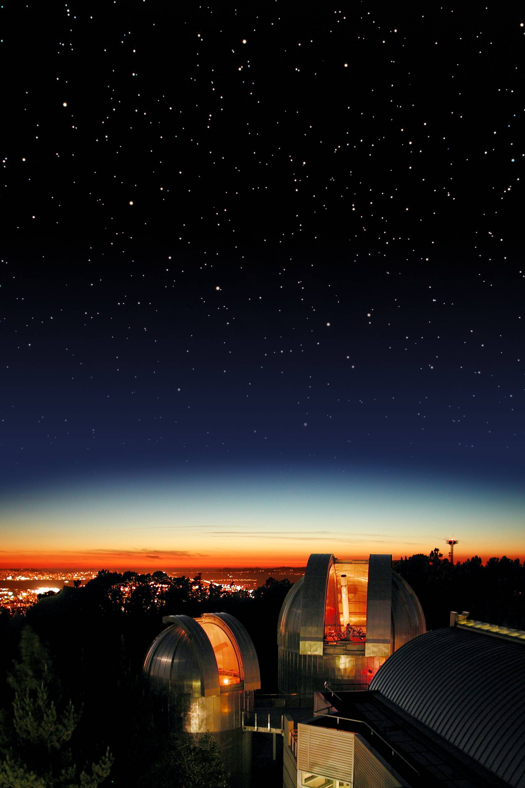 Bright dots scattered across the night sky, blue, orange and red sunset and a glowing orange round buildings. 