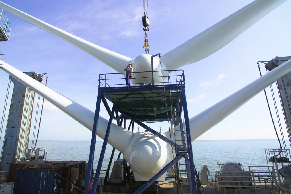A man stands on a platform in front of two white wind turbine propellers.