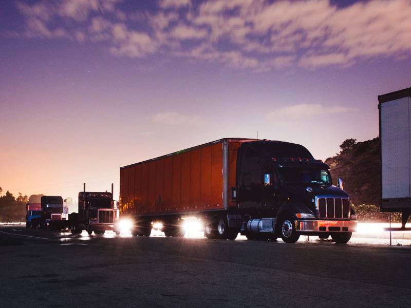 A line of semi-trucks in the foreground, with the sun setting in the background.