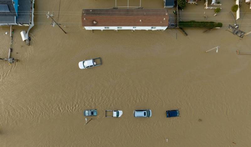 An aerial photo looking down on a house and cars. All are flooded with a mass of brown murky water. 
