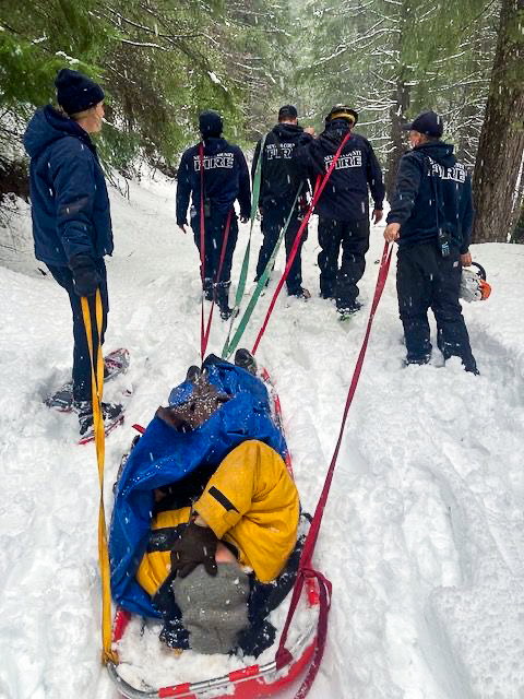 Five emergency workers pull a man wrapped in a blue tarp on a makeshift sled.
