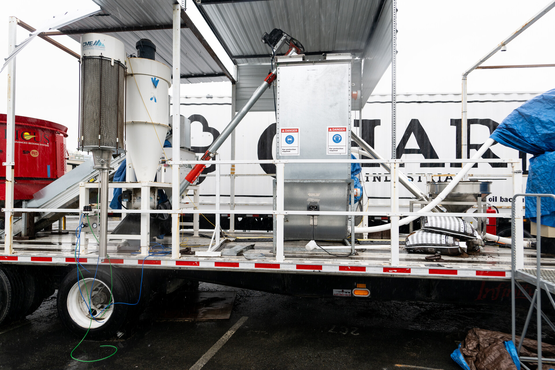A large white machine with various pipes and container sits on a flatbed truck. Behind it, a sign reads, 'Charm Industrial.'