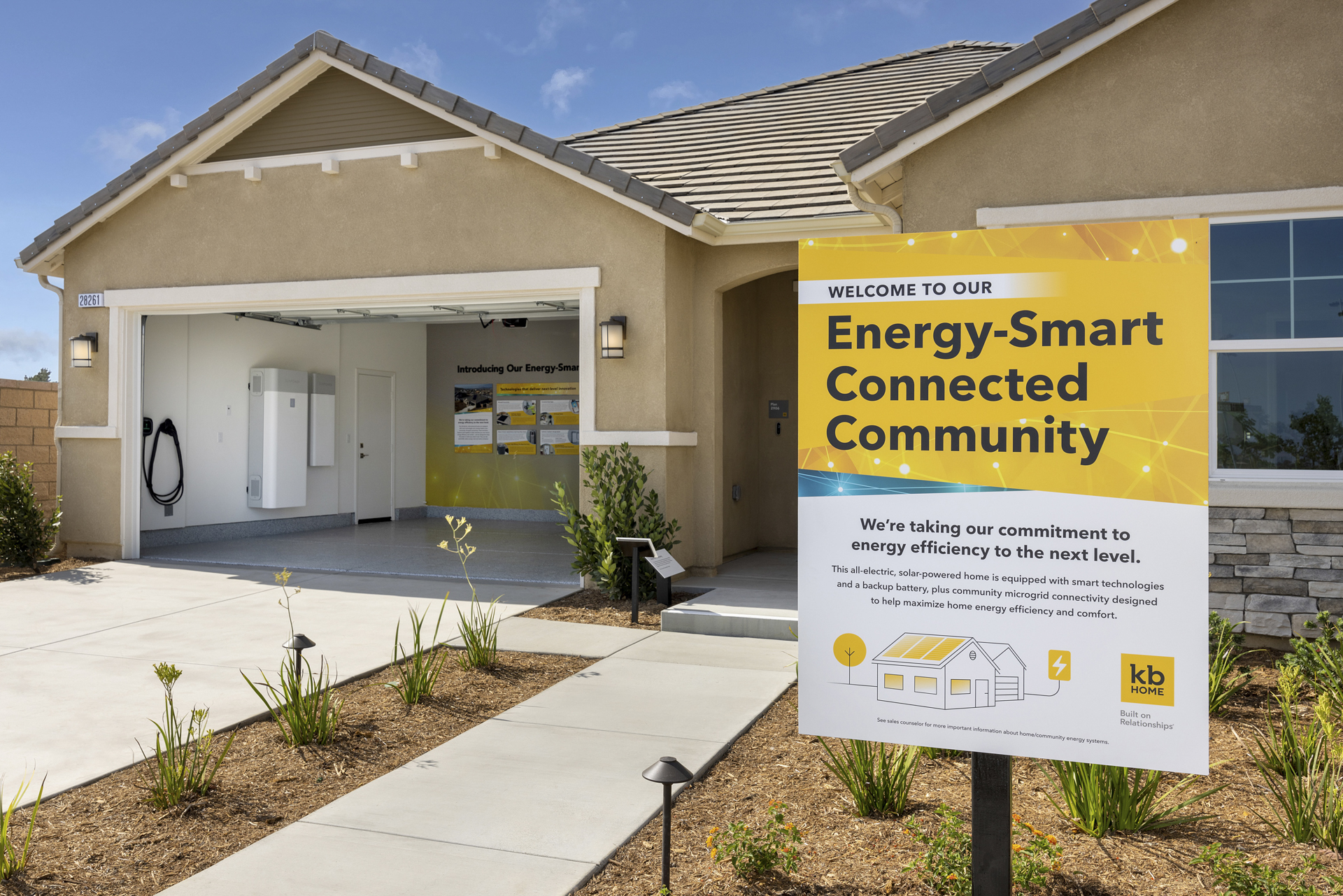 A tan house with a long driveway and a sign in its yard that reads, "Energy Smart Connected Community."
