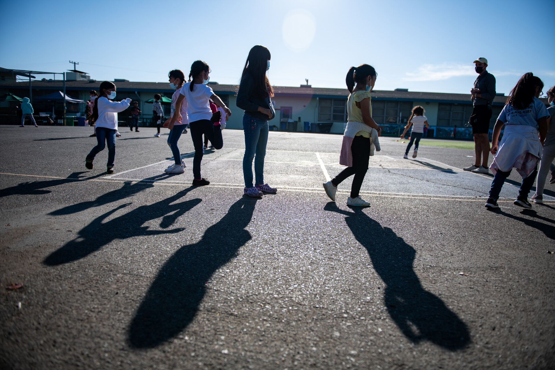 Children wearing masks play in a schoolyard on asphalt.