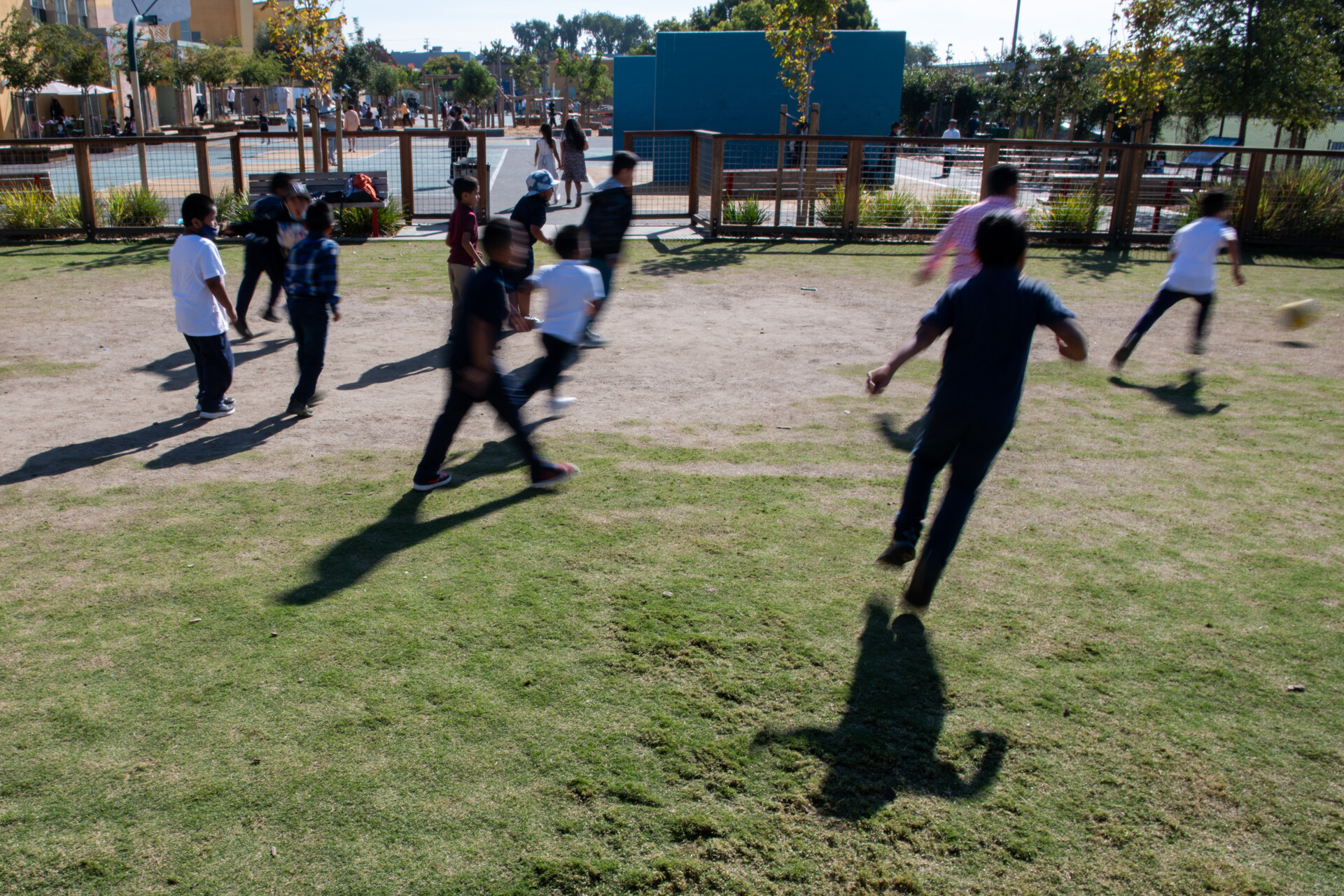 Children running after a soccer ball on a grassy school yard.