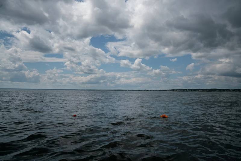 An orange float is seen floating in the dark ocean with clear blue and cloudy skies at the top.