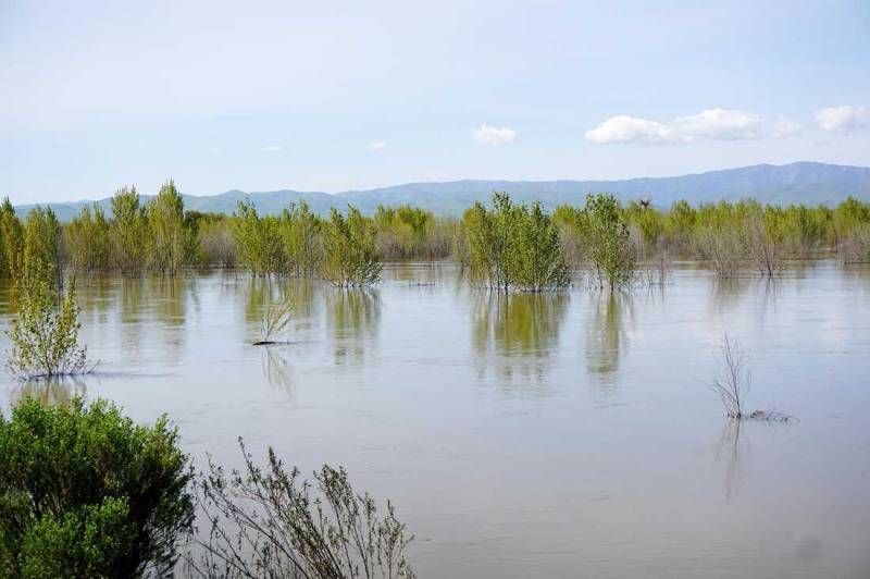 A floodplain is seen with mountains in the background, clouds and blue skies. 