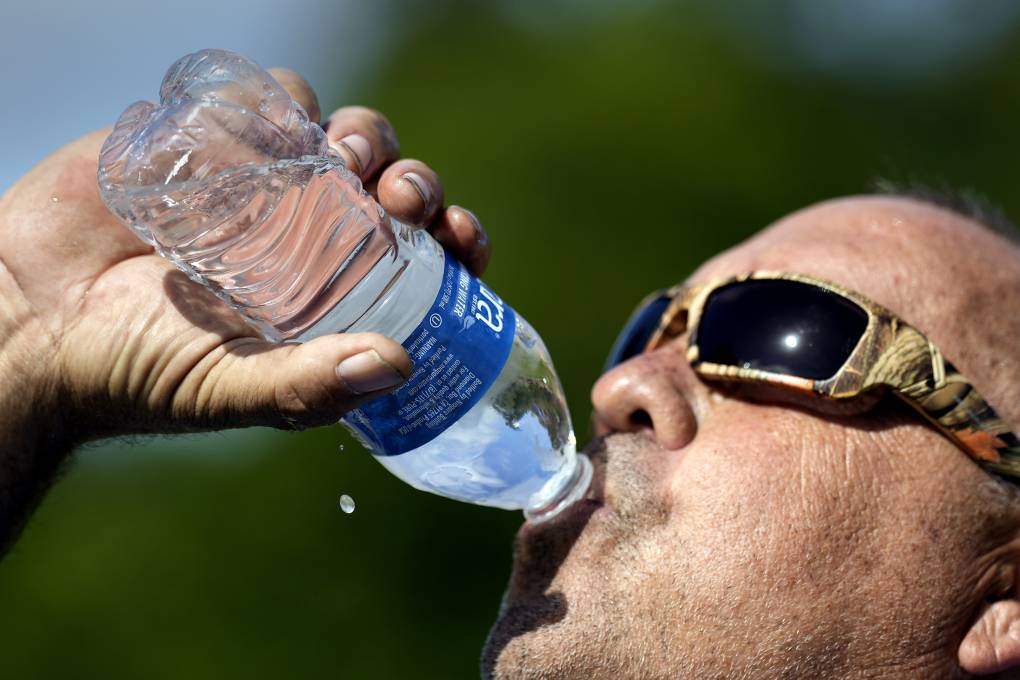 A man wearing sunglasses in drinking water from a plastic bottle.