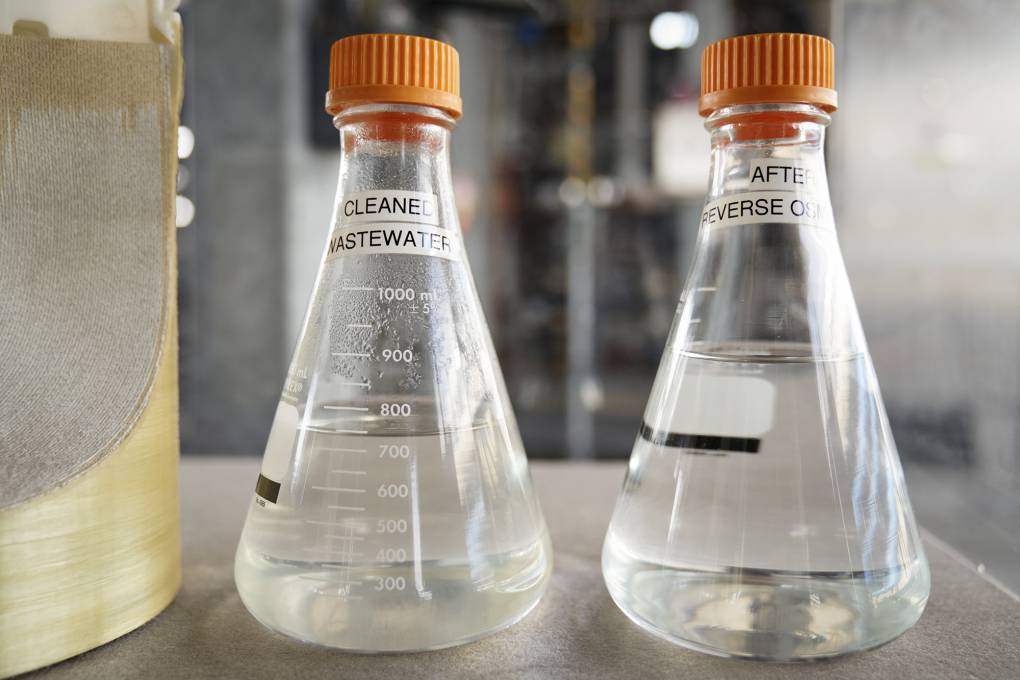 Two glass beakers are filled partially with water and have orange lids on. One beaker is labelled "Cleaned Wastewater" and the other "After Reverse Osmosis".