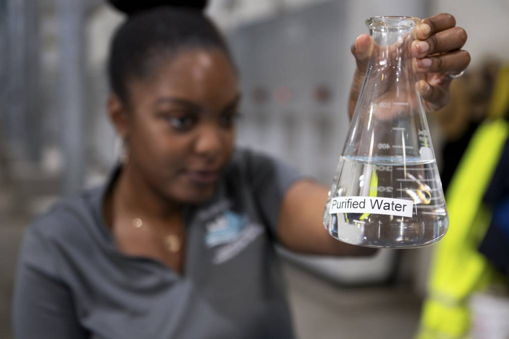 A person holds a beaker of clear liquid with a label on it that reads "Purified Water."