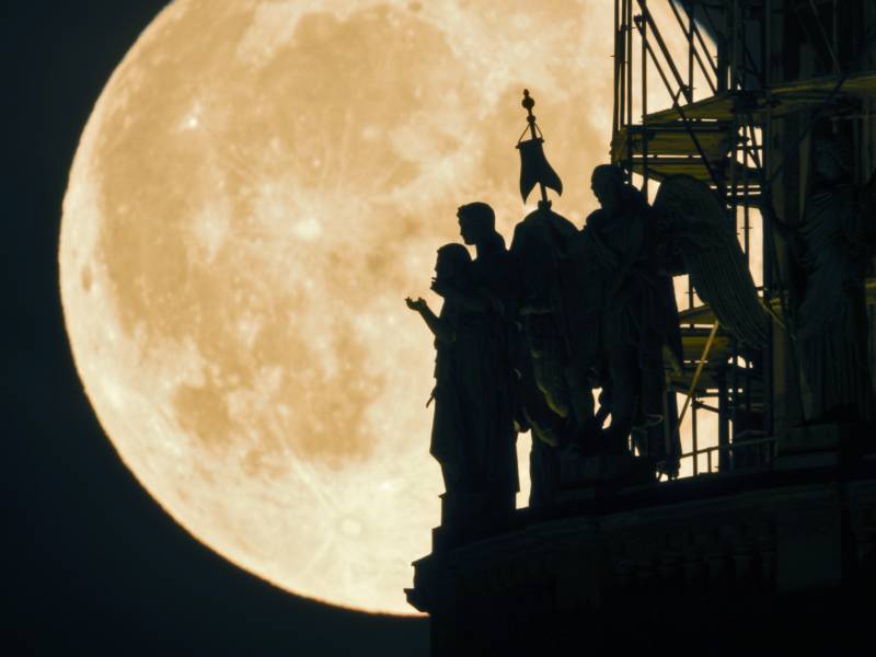 A bright full moon is seen here with a silhouette of angel statues.