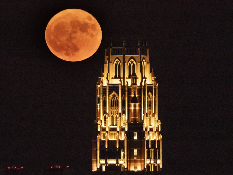 A bright orange full moon is seen in the background. In the foreground, a tower is lit up.