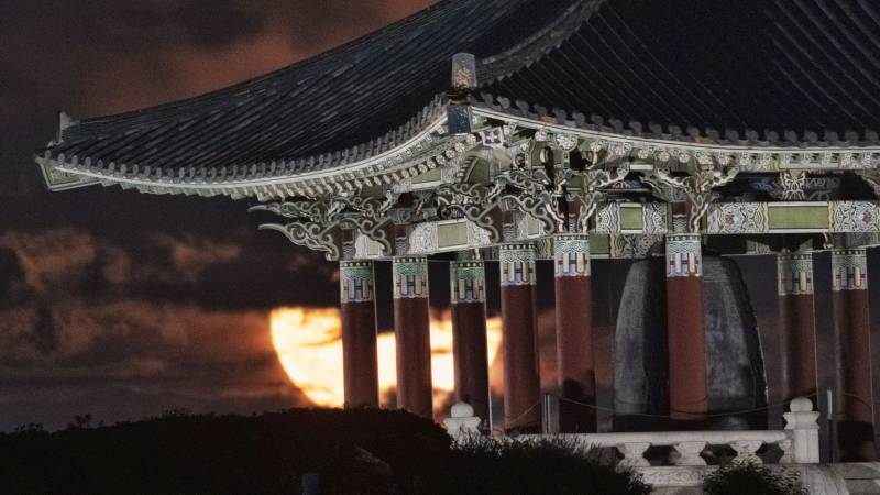 Behind a temple, a bright full moon is shining amongst dark clouds. 