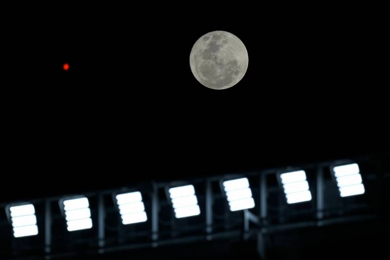 A bright full moon appears in the dark sky. Bright lights from a stadium are also seen in this photo. 