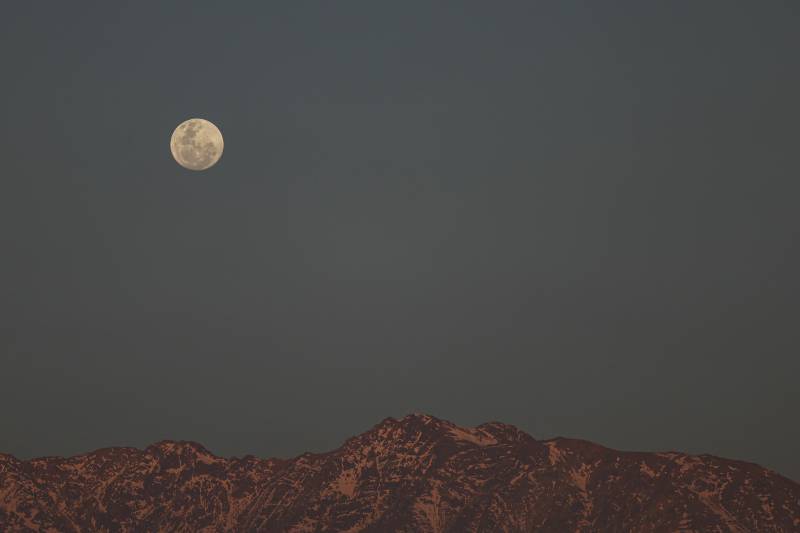 A bright full moon is seen rising behind the mountains. 