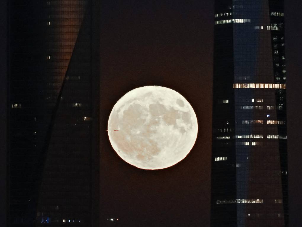 An image of a bright and glowing moon is seen in between two buildings.