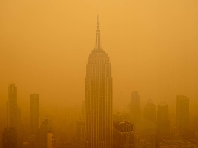 Orange skies and smoke is seen in a city amongst buildings.