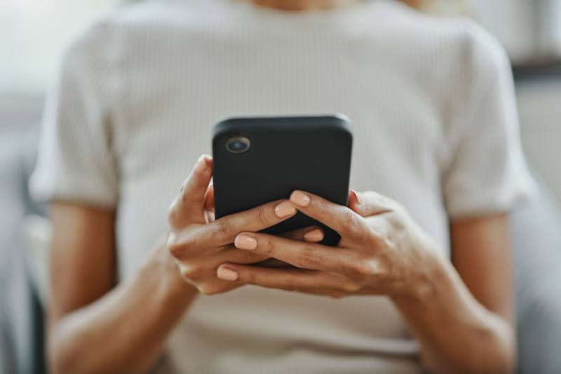 A woman wearing a white shirt holds a cellphone in her hands.