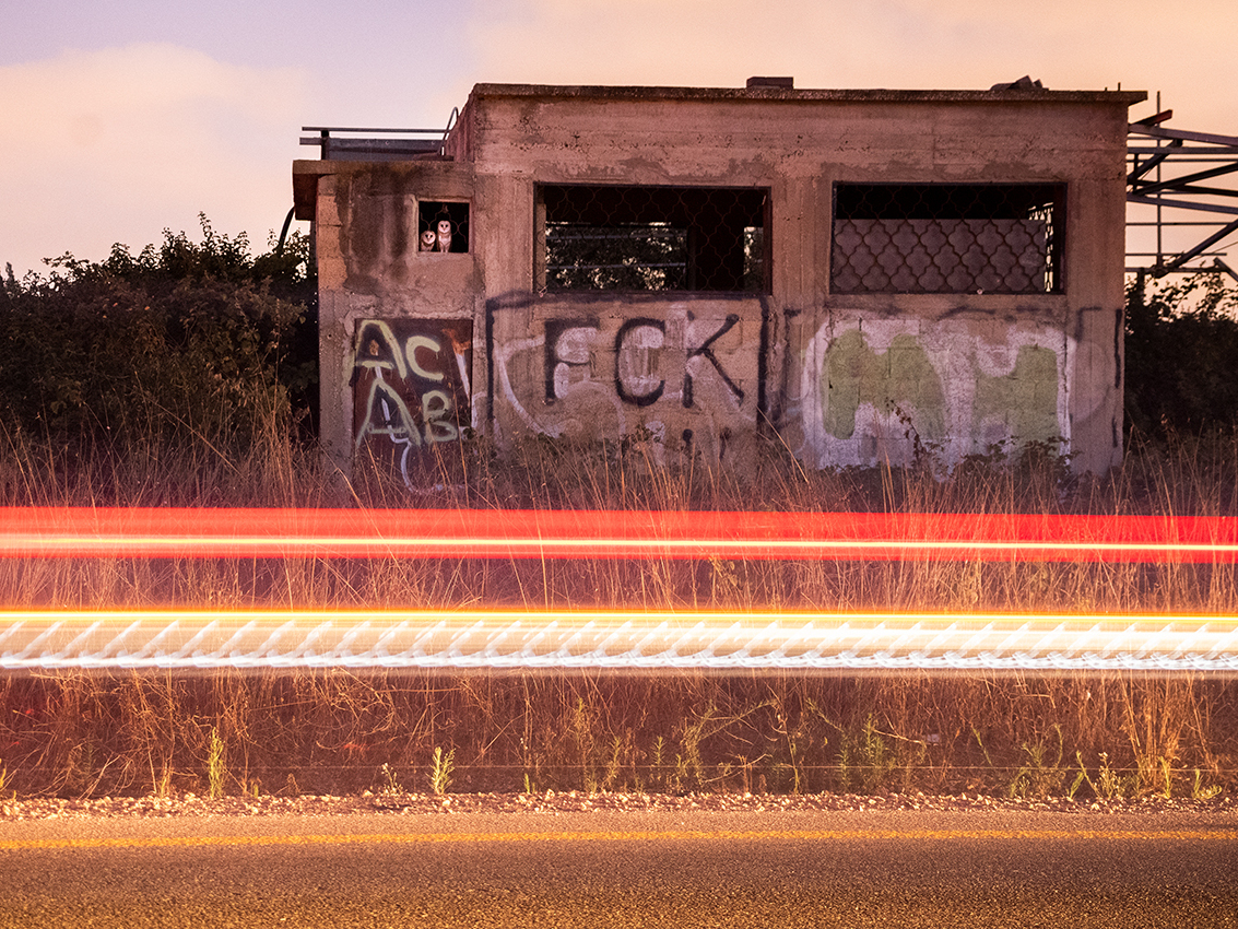 Two owls are seen perched in a window of an abandoned building. Graffiti is seen on the building. Red, yellow, and orange lights are seen in front of the building.