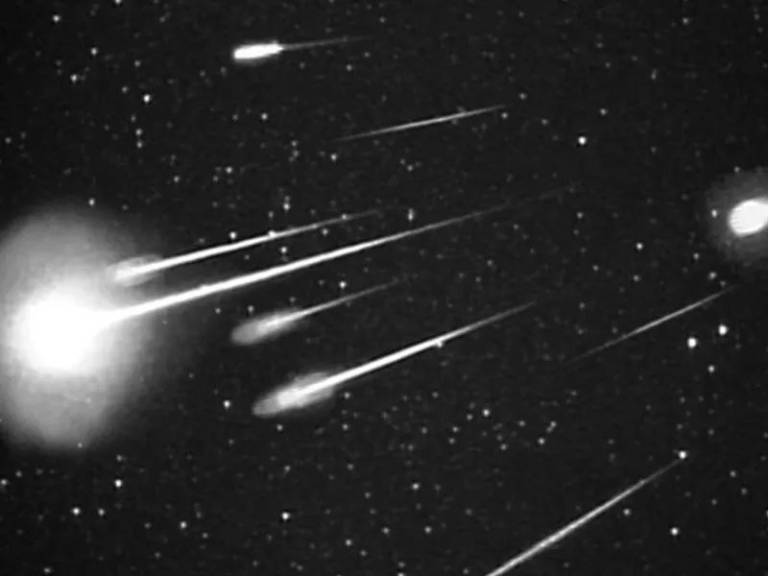 Meteors flash as white lights on a black background in the sky.