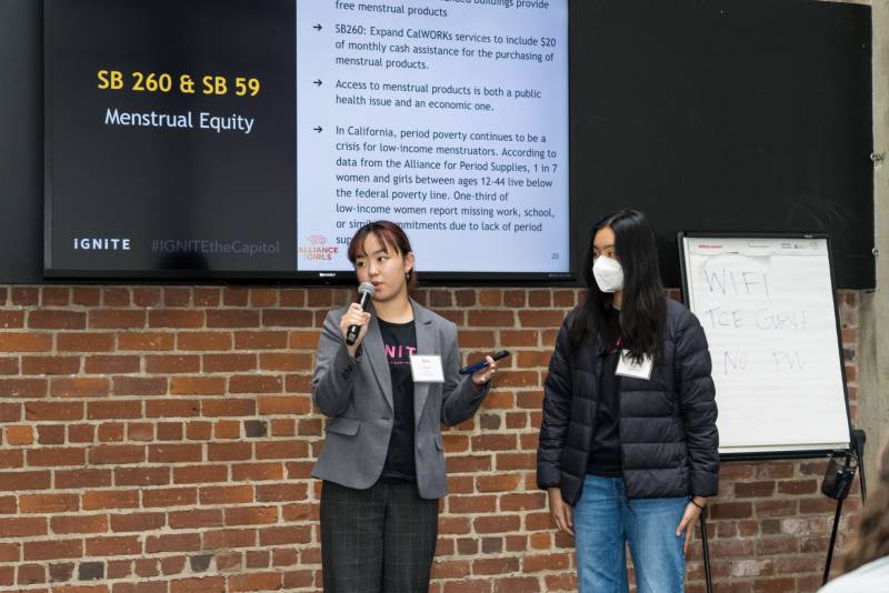 Two young Asian women stand behind a digital display that reads "SB 260 and SB 59."