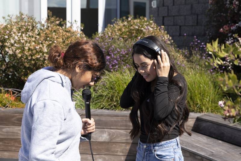 Two teenage girls record audio with microphone and headphones standing in a garden