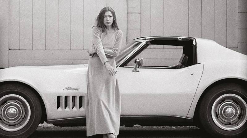 Joan Didion leans against a car