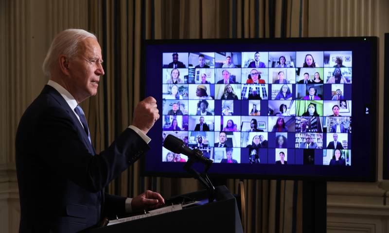 Joe Biden standing behind a podium while facing a screen, virtually swearing in his new administration