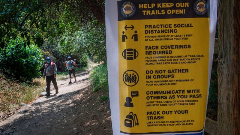 Hikers walk through trail with masks on while signs of social distancing are put up