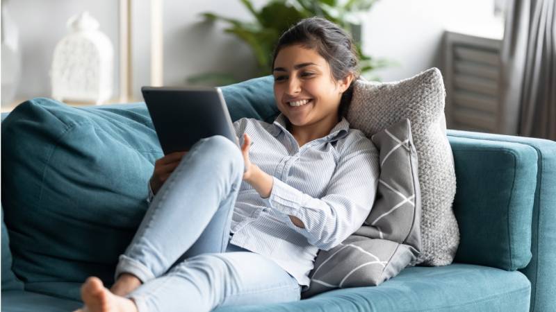 A girl lies on her couch and smiles at an iPad in her hands