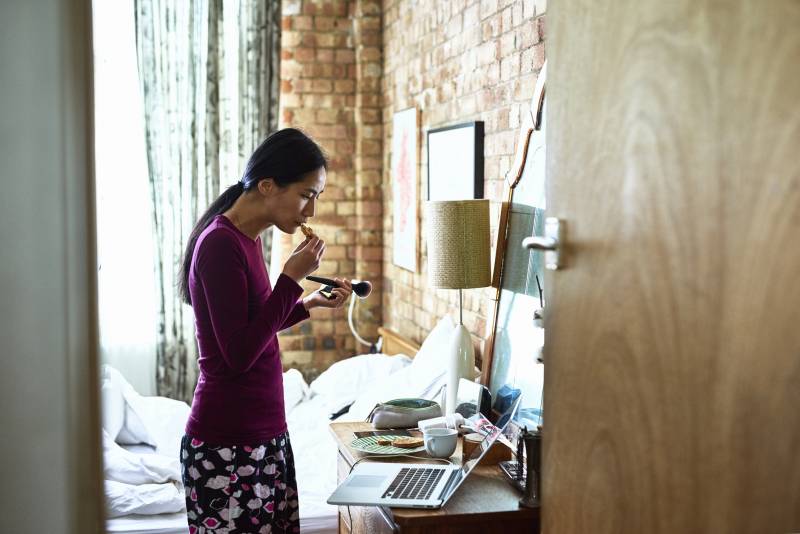 A woman standing in her bedroom multi-tasking