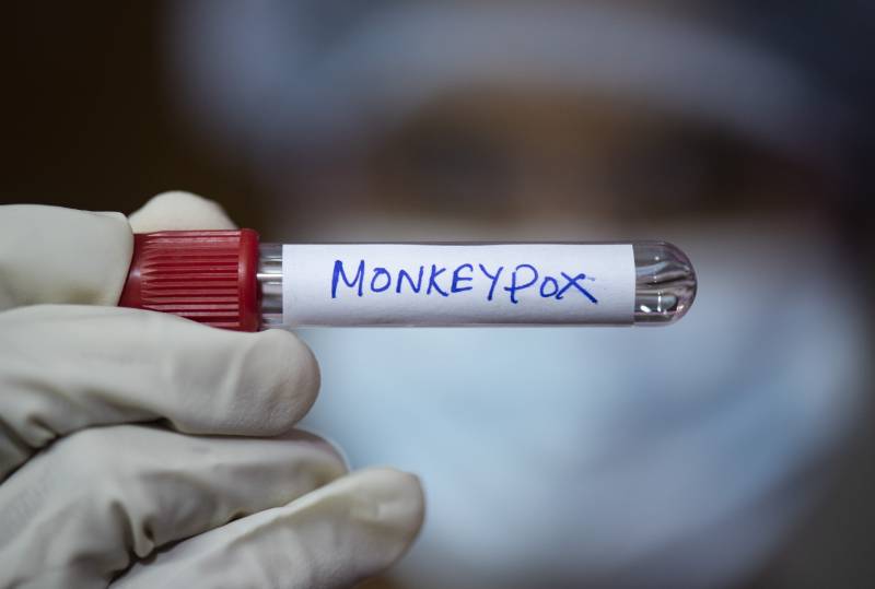 A health worker wearing gloves holding a test sample tubes labeled 'Monkeypox'.