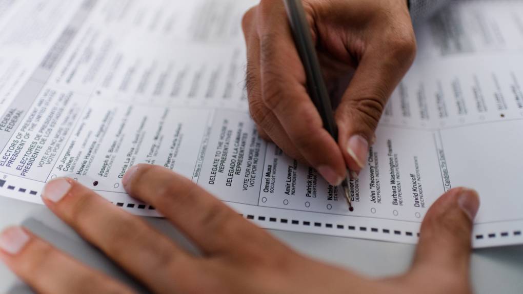 A close up of a man's hands completing absentee ballot for an election.