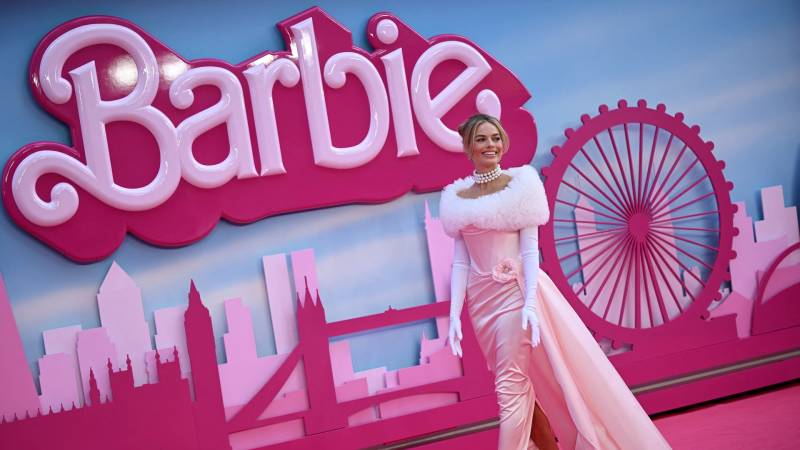 Margot Robbie posing for cameras in front of Barbie background.
