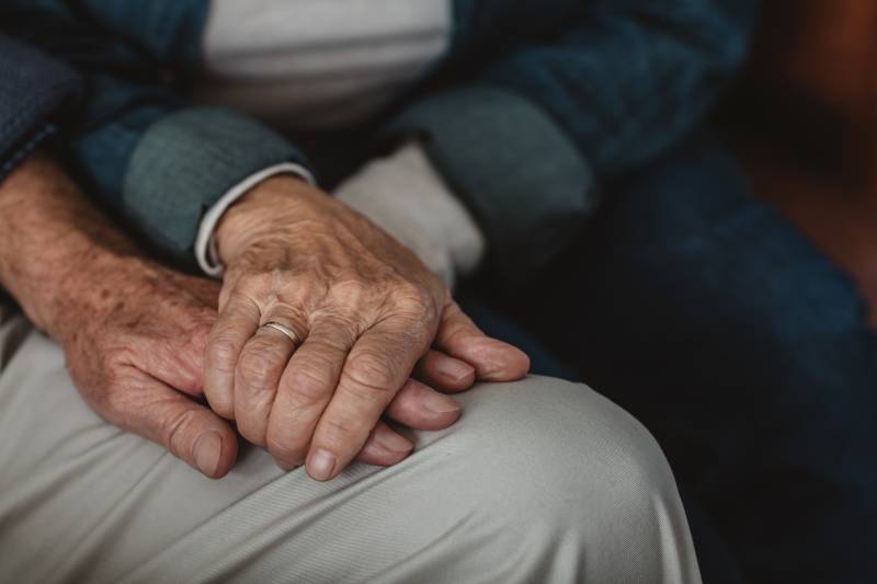 Closeup of a senior couple holding hands while sitting together on their living room sofa at home