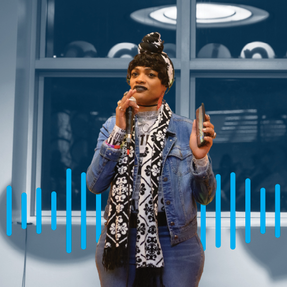 A woman with a headwrap talking into a microphone set to a blue background