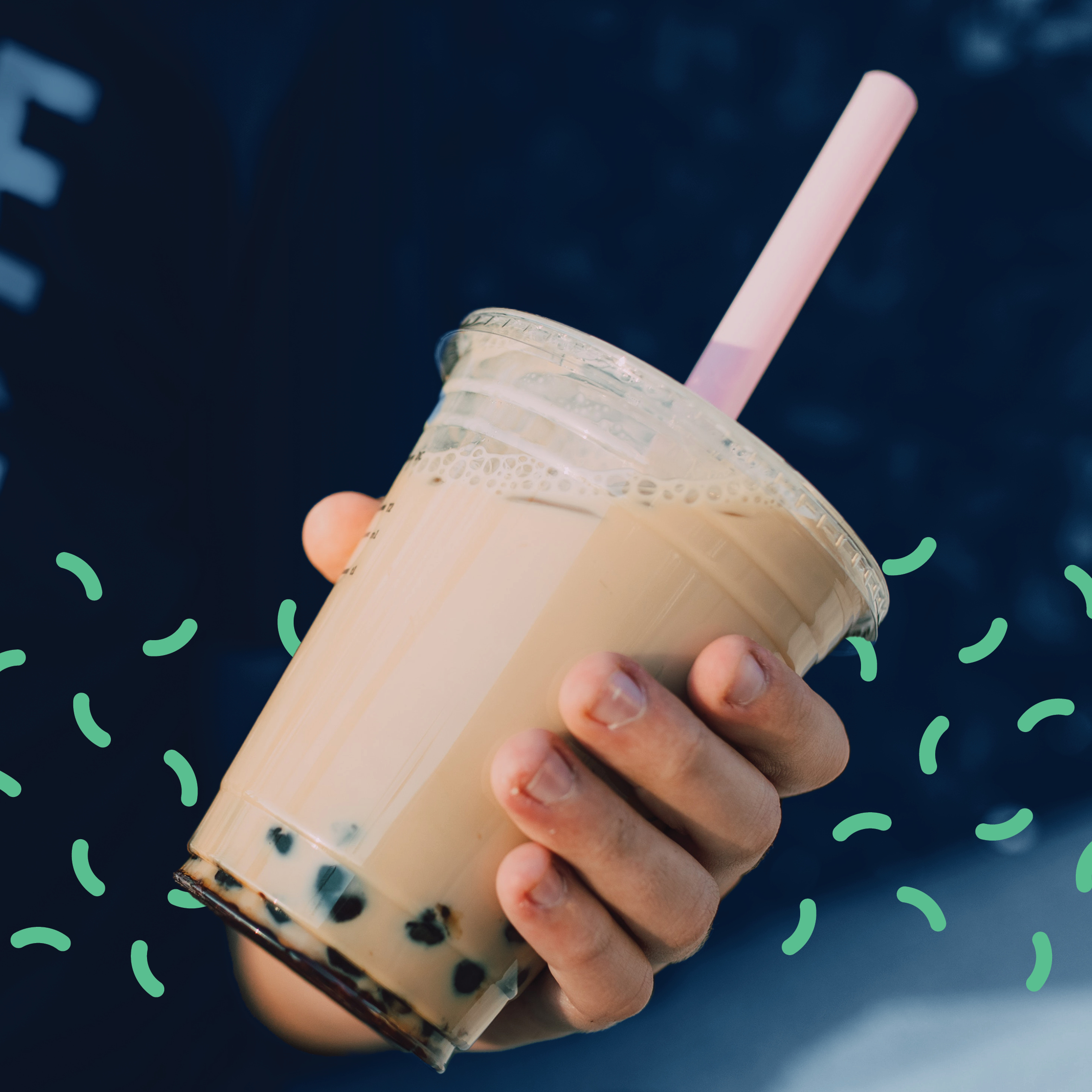 A hand holding a cream colored cup of milk tea with boba at the bottom.
