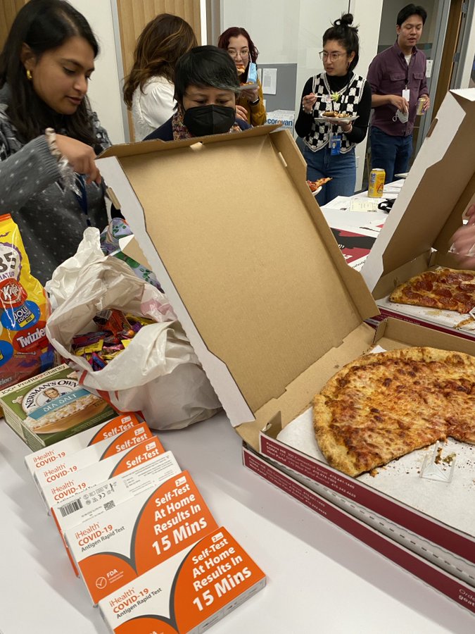 Pizza sits on a white table surrounded by people eating it. 