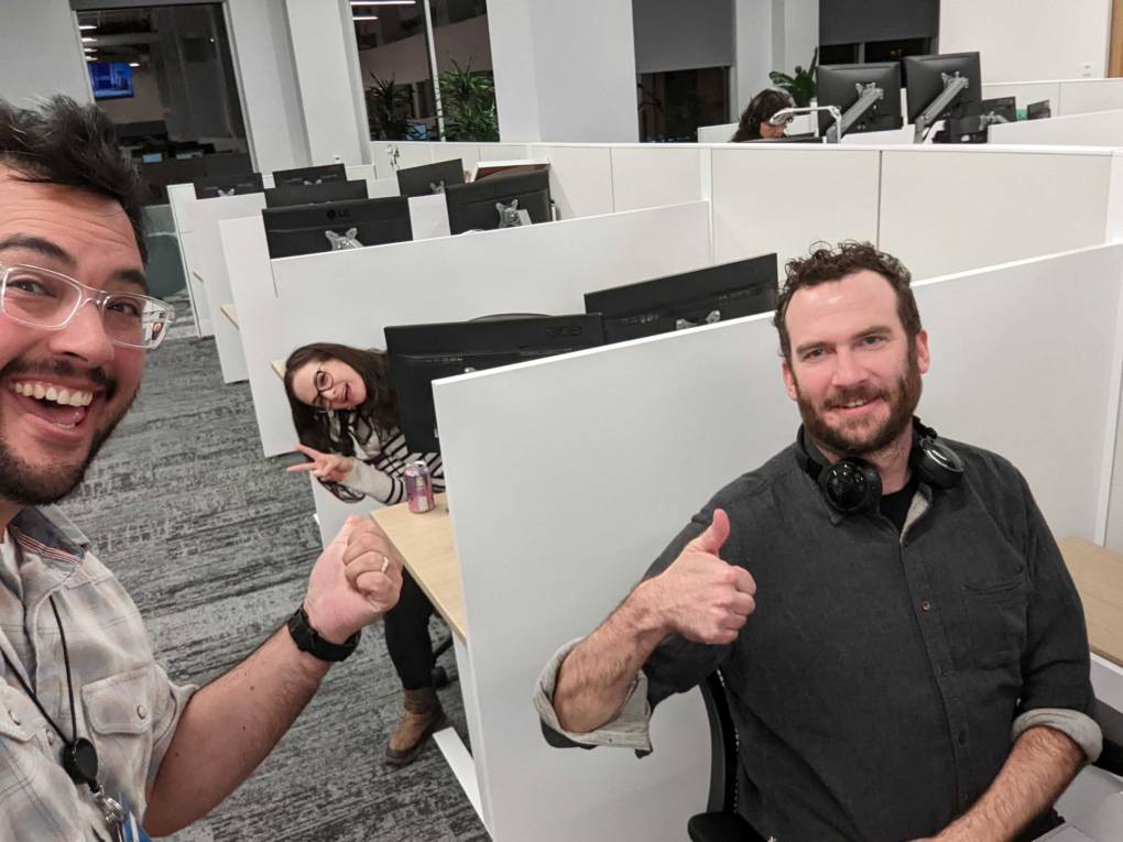 Three people give thumbs up and smile for a photo in an office. 