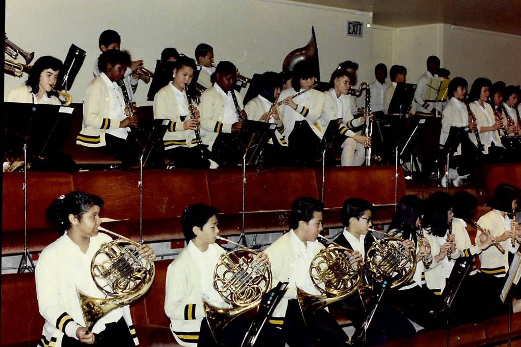 A group of young people in uniforms play musical instruments in an indoor location.