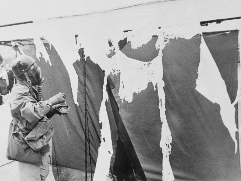 Metzger wears a gas mask while painting three nylon curtains with hydrochloric acid, causing them to disintegrate, in 1961