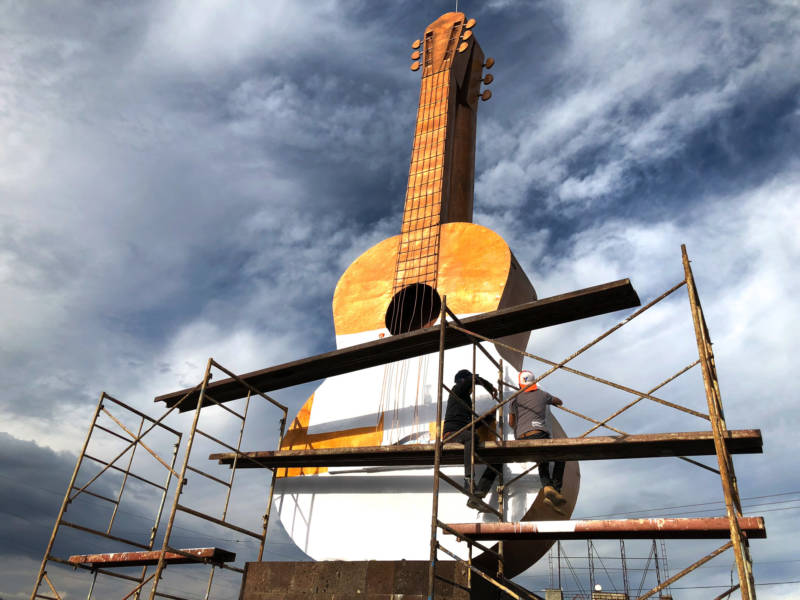 Workers cover a large bronze guitar statue in white. The statue sits at the entrance to the town of Paracho. This weekend, the town will pay tribute to German Vazquez, a former resident and master guitar maker from the town. Vazquez designed the white guitar featured in the movie <em>Coco</em>.
