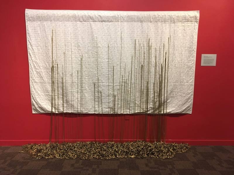 "Mending Gold: When Will It Be Enough?" 2017 by Brooke Harris-Stevens. Each thread anchored into the brass casings signifies the number of mass shootings in an American city.