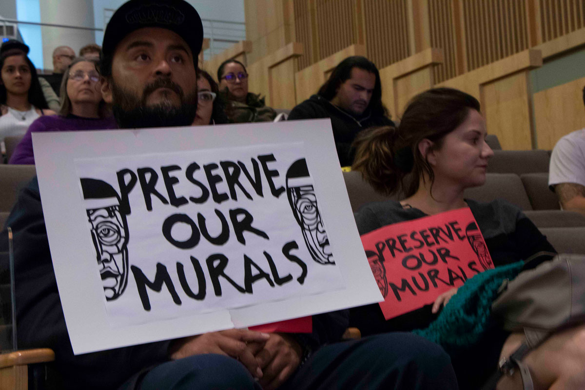 Residents Juan Carlos Araujo and Maricela Lechuga hold up signs urging the Historic Landmarks Commission to help protect Chicano murals at City Hall in San Jose, on Oct. 2, 2019.
