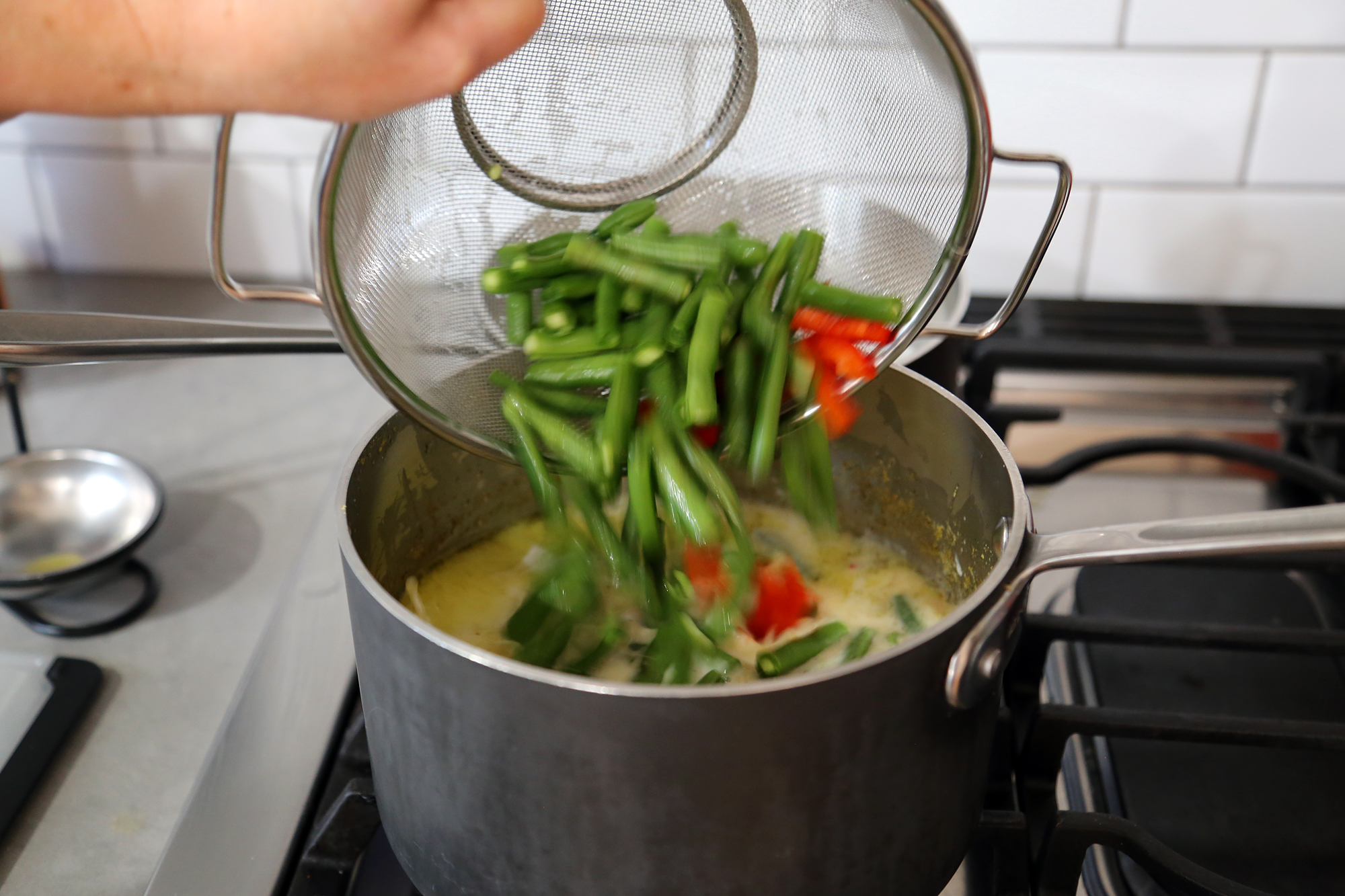 Add the coconut milk, green beans, bell pepper, and green onions to the saucepan. 