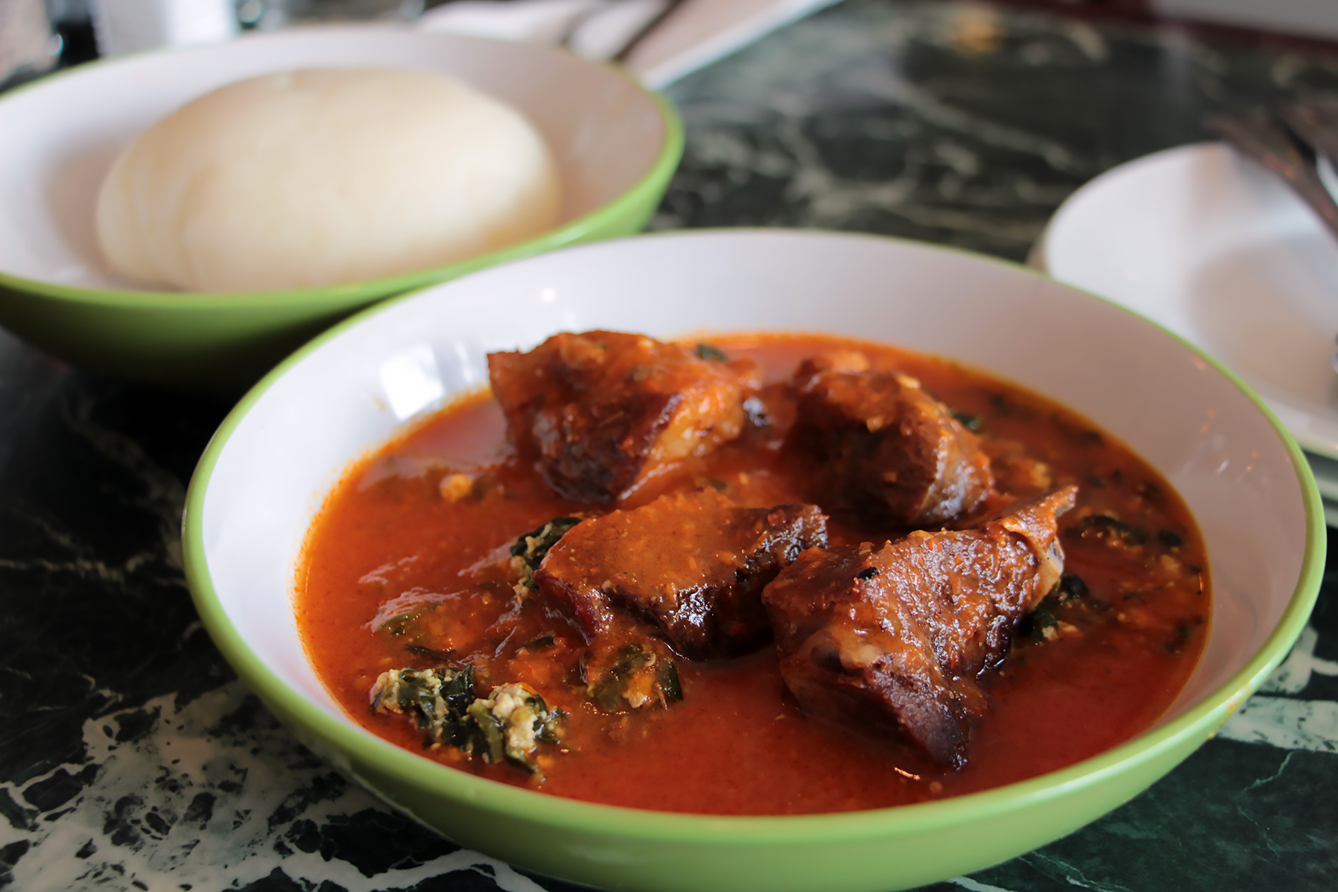Goat served on the bone in the rustic, chunky tomato and spinach stew with mashed egusi. Served with Fufu.